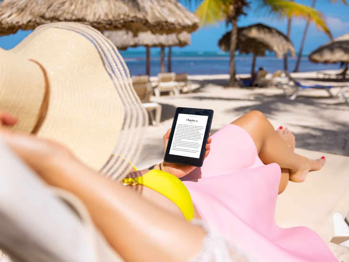  A person relaxing on a beach chair under a straw umbrella, holding a Kindle e-reader. Don’t forget to add an e-reader to your California packing list to enjoy some reading time while soaking up the sun at the beach.