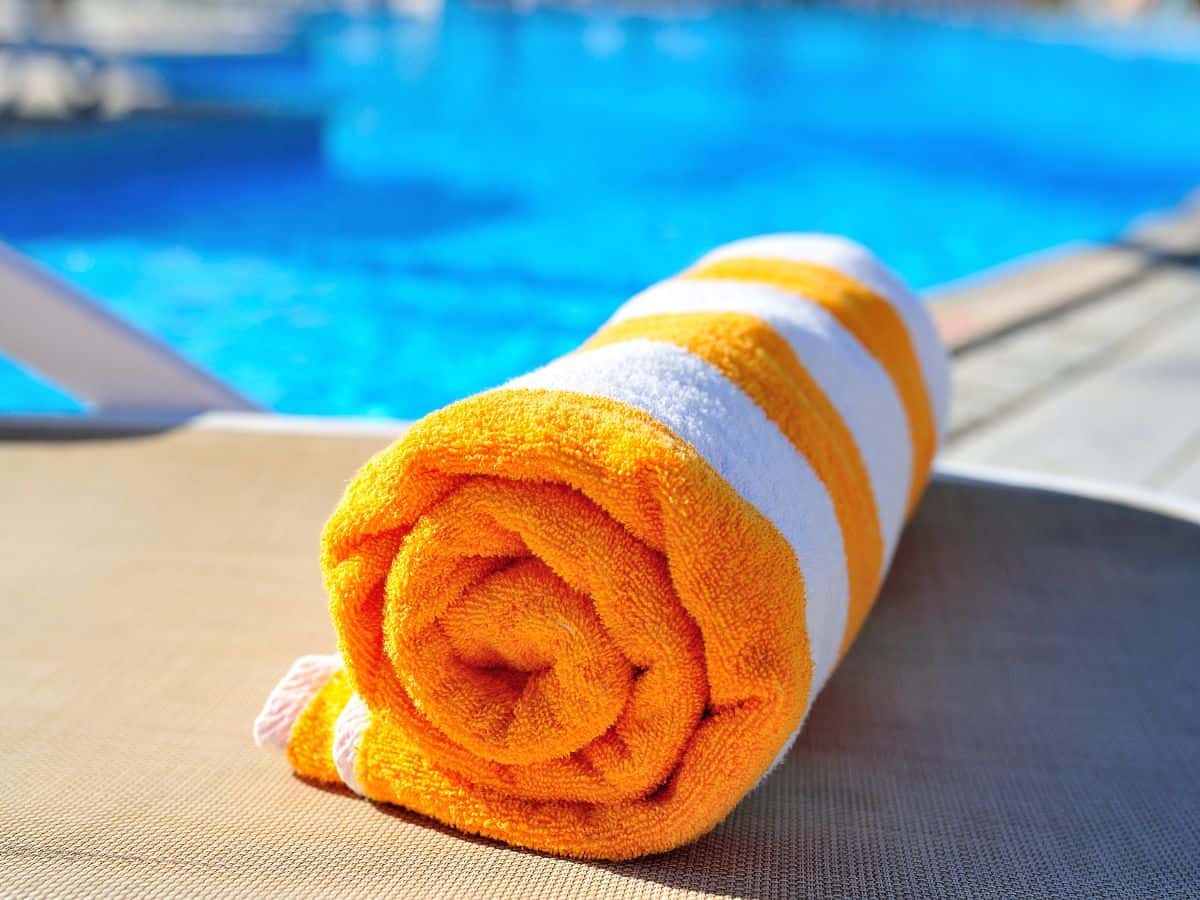 A rolled-up orange and white striped beach towel placed on a poolside chair, with the pool water in the background. Don’t forget to add a beach towel to your California packing list for a relaxing day by the water.