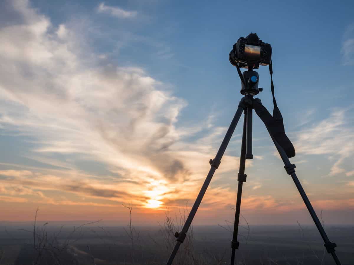 A camera mounted on a tripod, capturing a beautiful sunset. A sturdy tripod is an essential item on your California packing list for capturing stunning landscape photos.
