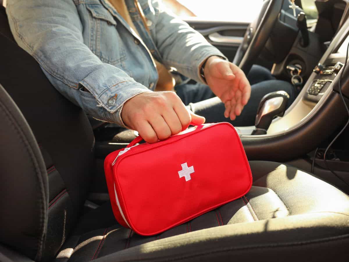 A person holding a red first aid kit inside a car. A first aid kit is an important part of any California packing list, ensuring you're prepared for minor injuries on the road.