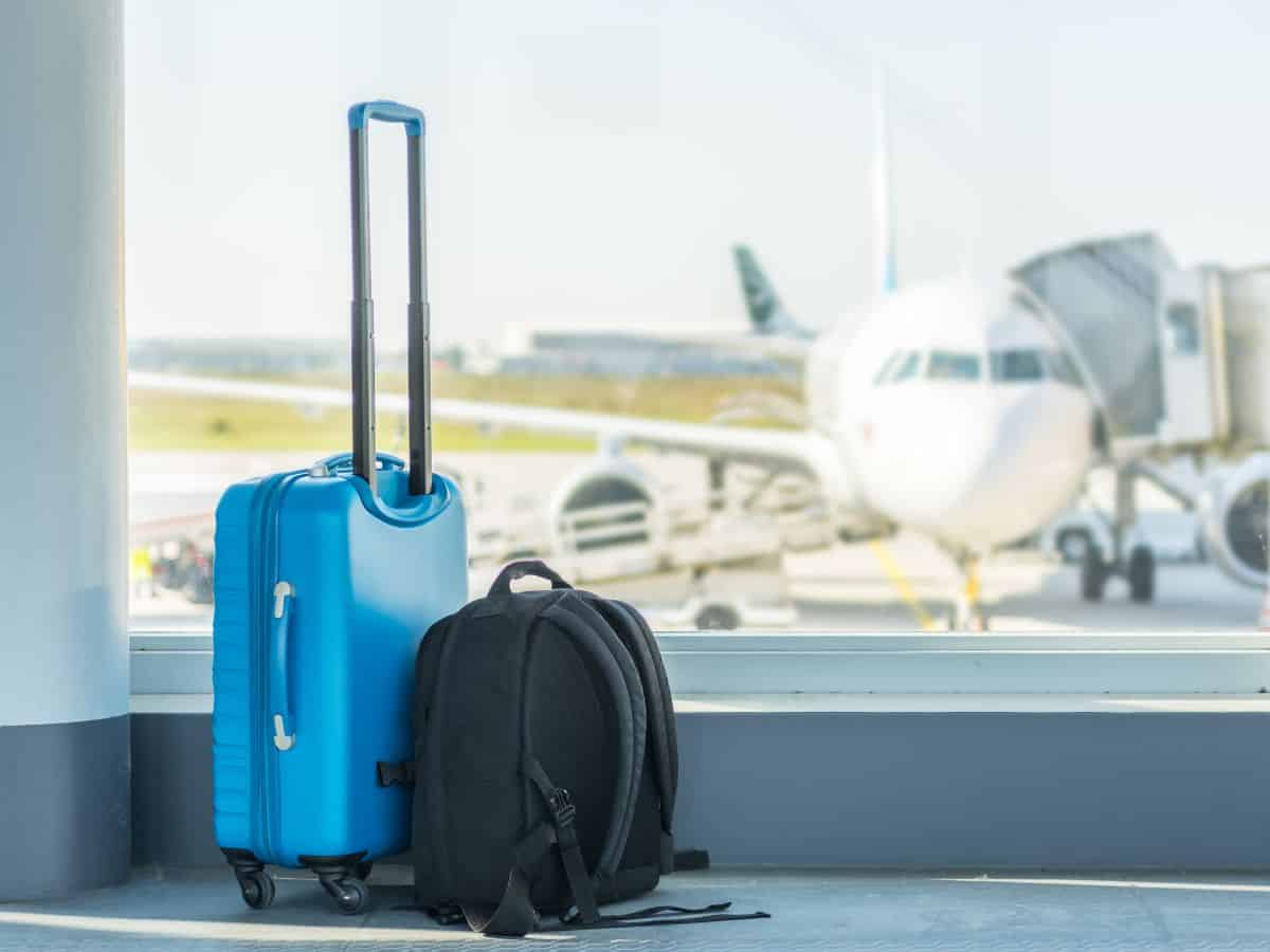  A blue carry-on suitcase and a black backpack placed in an airport terminal, showcasing the importance of efficient carry-on luggage for your California packing list.