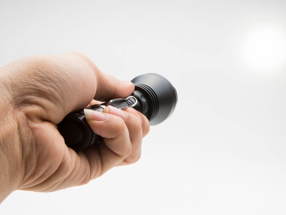 A close-up shot of a hand holding a black emergency flashlight, illuminating the area. Essential for any California packing list, especially for road trips or emergency situations.