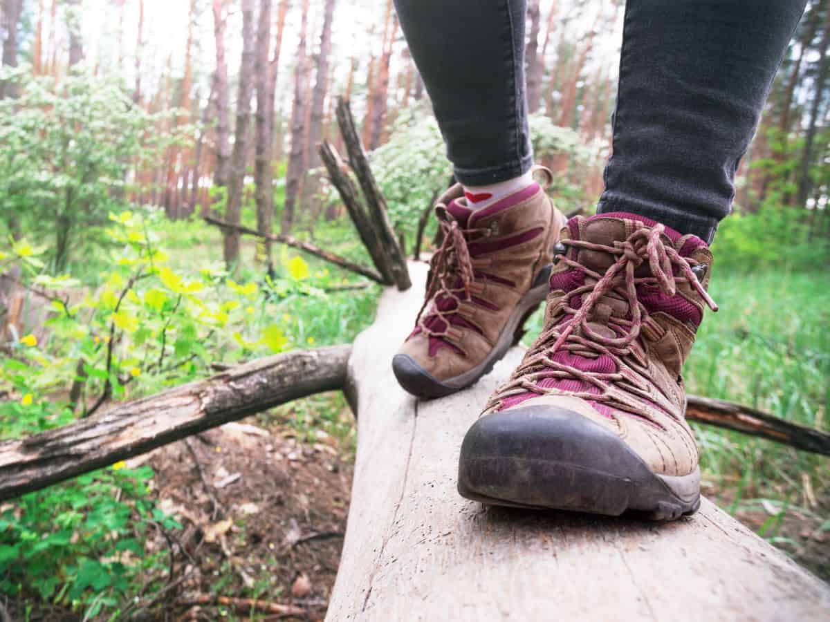 A close-up of a person wearing sturdy hiking boots while balancing on a log in the forest, showcasing the necessity of durable footwear in the California Packing List for outdoor adventures.