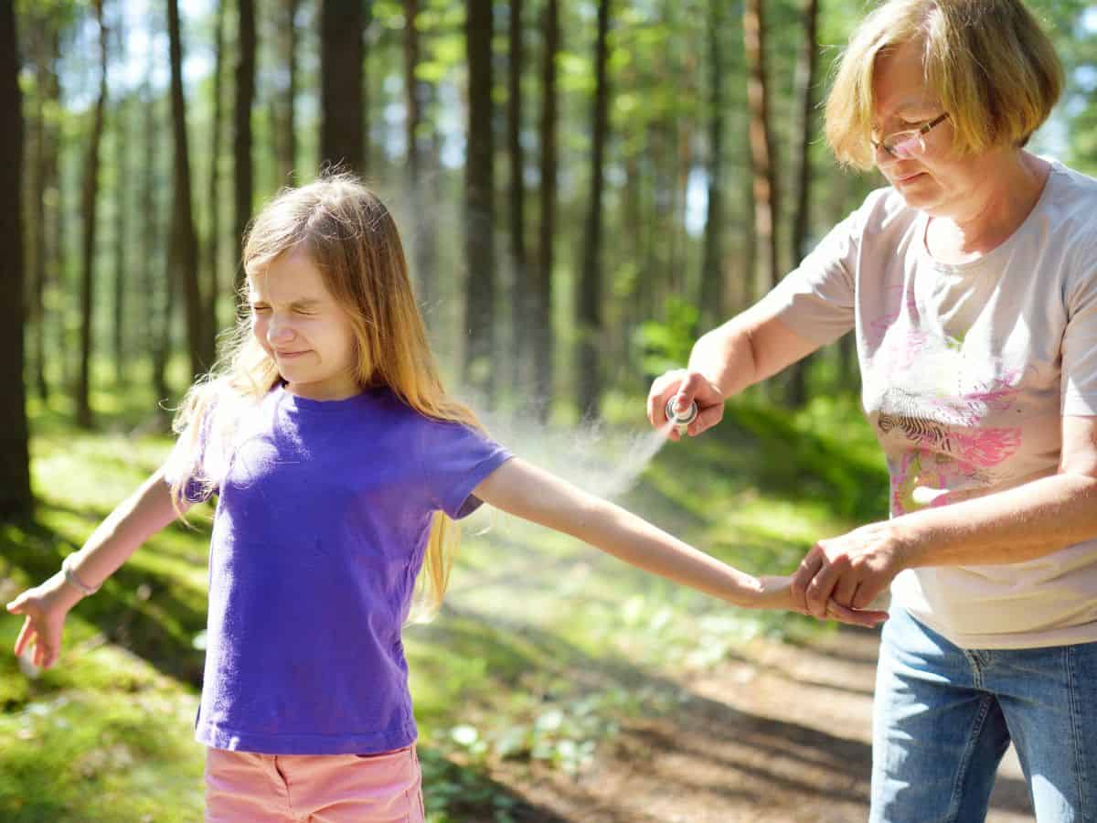 An adult spraying insect repellent on a child’s arm while in a wooded area. Insect repellent is a critical item on your California packing list to avoid bug bites during outdoor adventures.