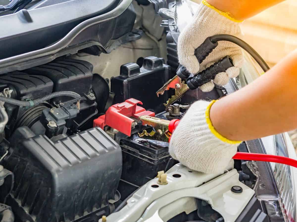 A person using a jumpstart kit to connect to a car battery. A must-have item on your California packing list for roadside emergencies.