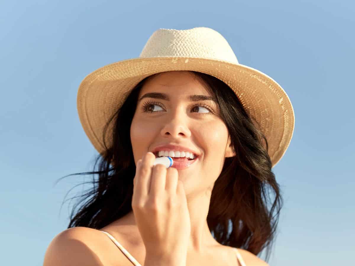 A woman applying lip balm while wearing a sunhat, an essential in the California Packing List for protecting lips from the sun in California's sunny weather.