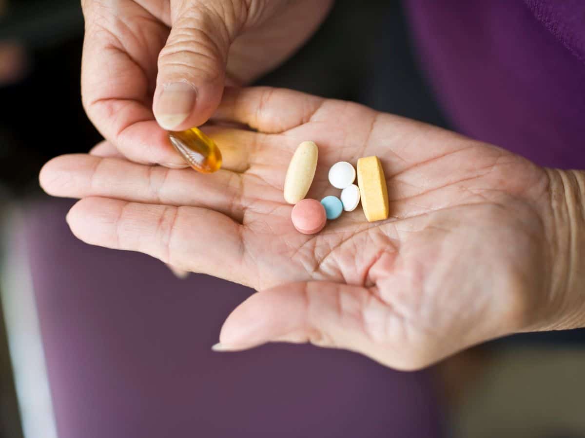 A close-up of a hand holding various medications, including pills and supplements. Ensure your medications are part of your California packing list to maintain your health during your travels.