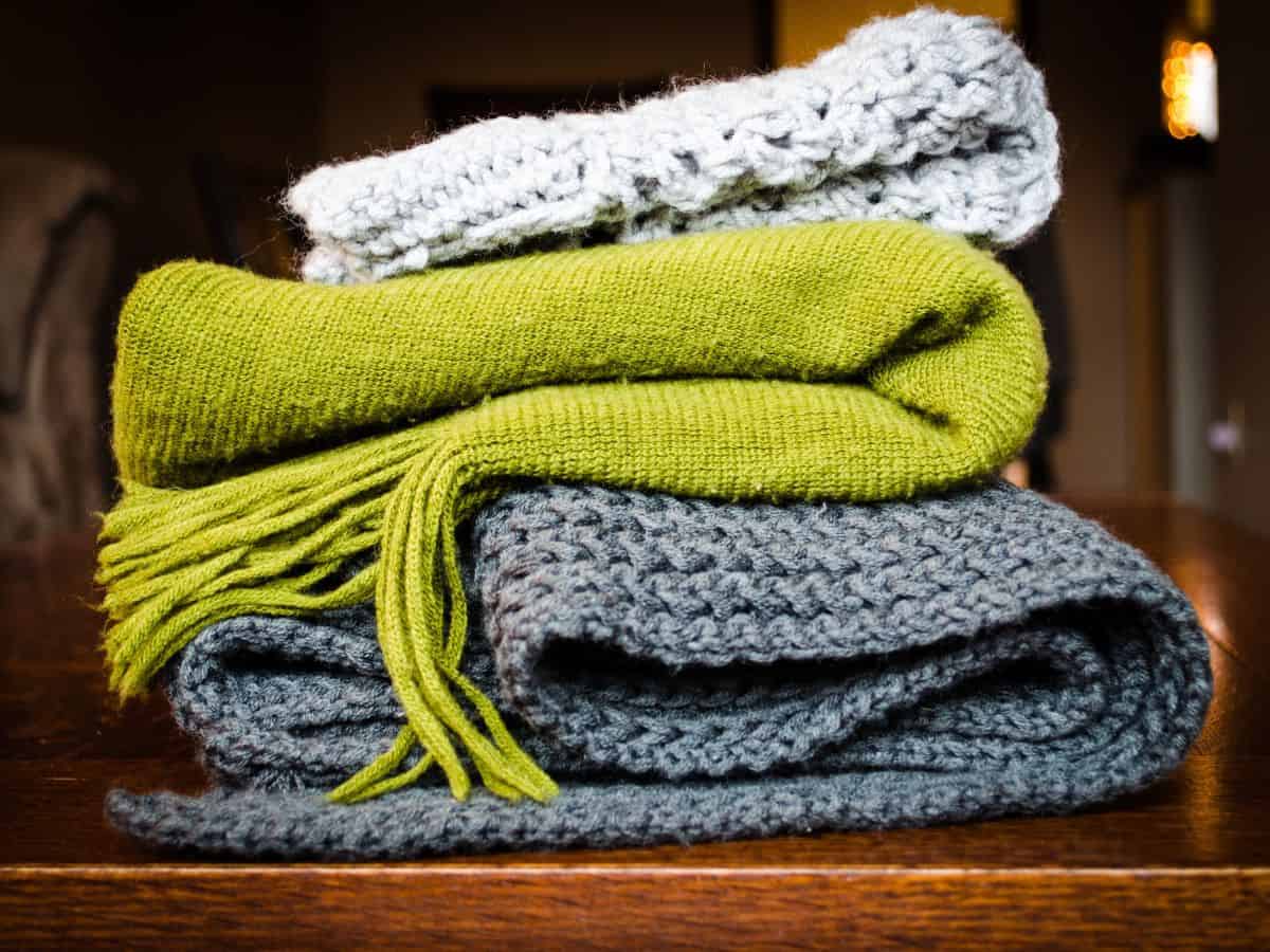  A stack of knitted scarves in various colors, suggesting that a cozy scarf is a smart addition to your California packing list for layering during brisk weather.