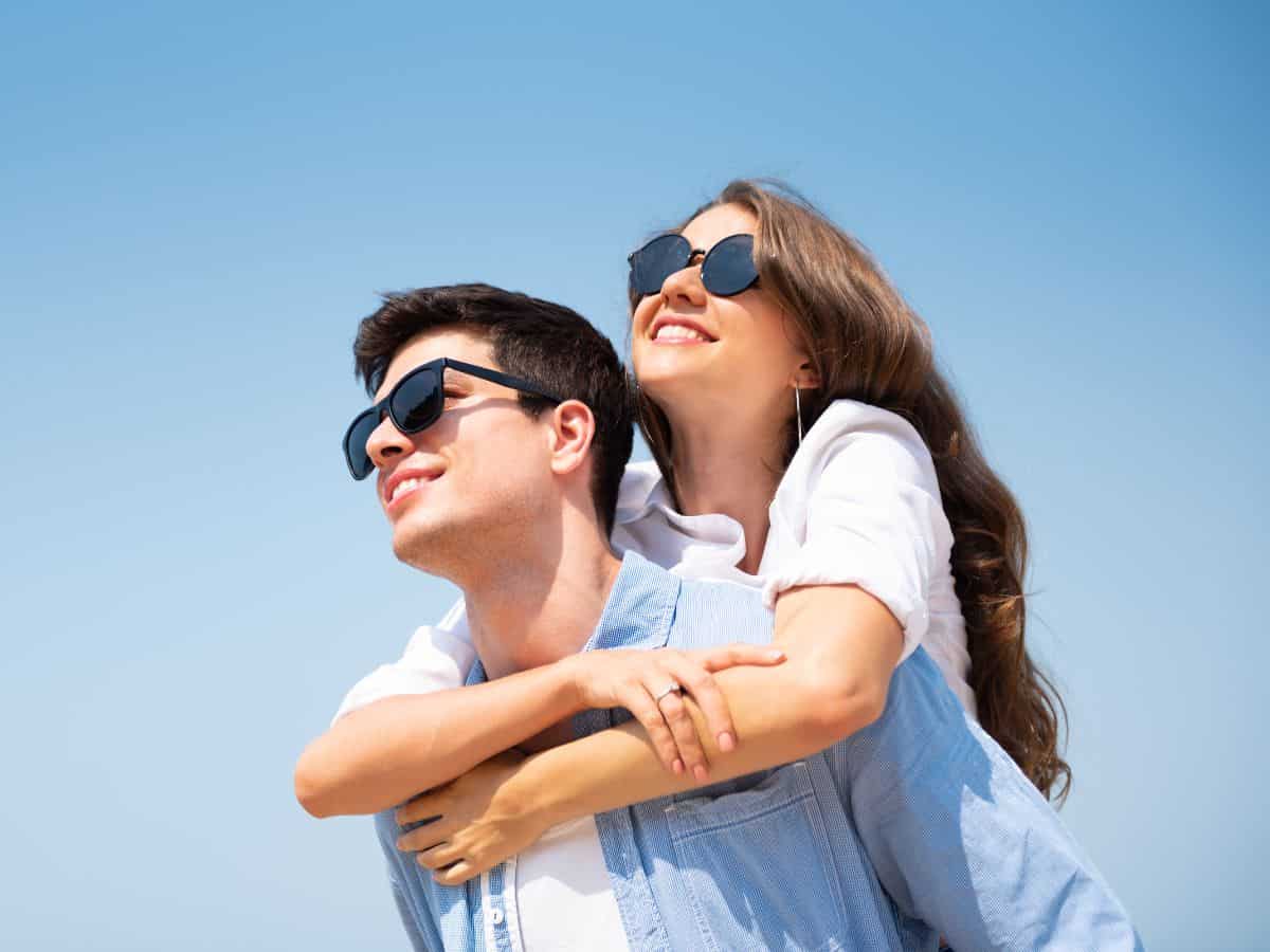A couple wearing sunglasses, smiling under a clear blue sky. Sunglasses are a must-have item on your California packing list to protect your eyes from the bright California sun.

