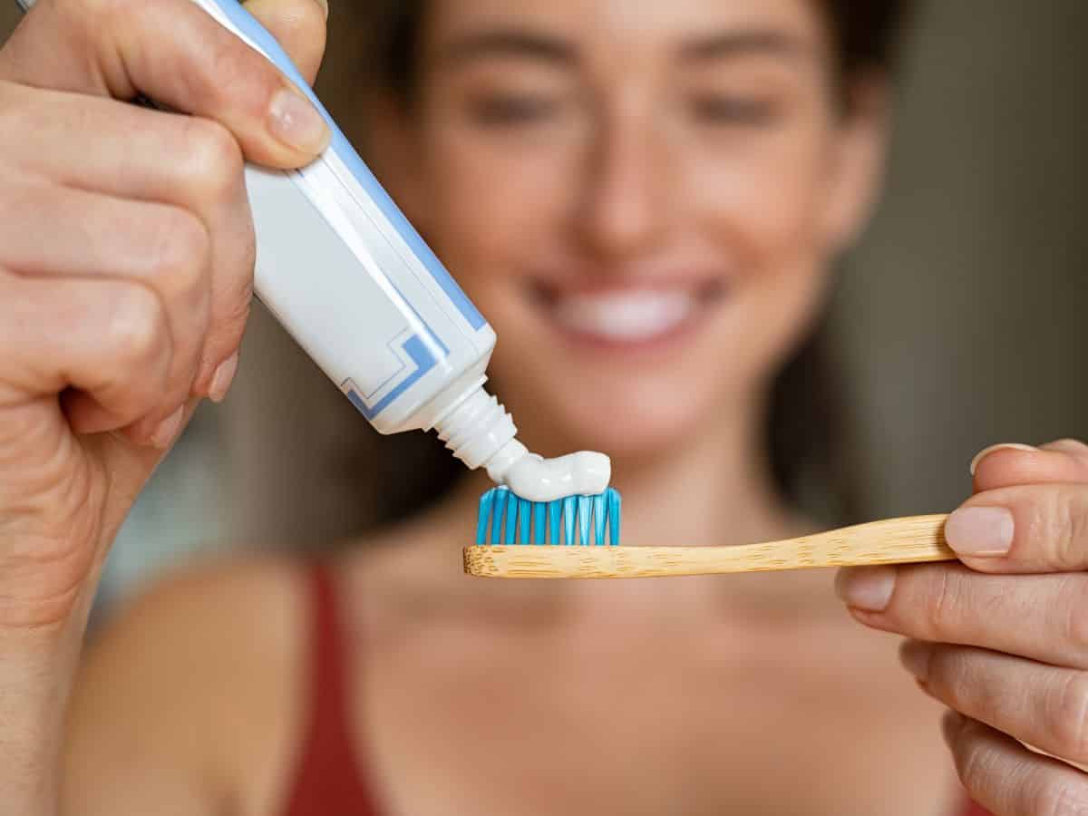 A person squeezing toothpaste onto a bamboo toothbrush, emphasizing a crucial item in the California Packing List for maintaining oral hygiene during trips.