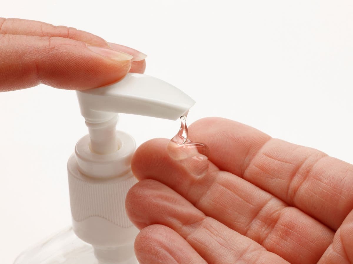 A person dispensing a small amount of hand sanitizer gel onto their palm from a pump bottle, an essential item on the California Packing List for maintaining hygiene on the go.