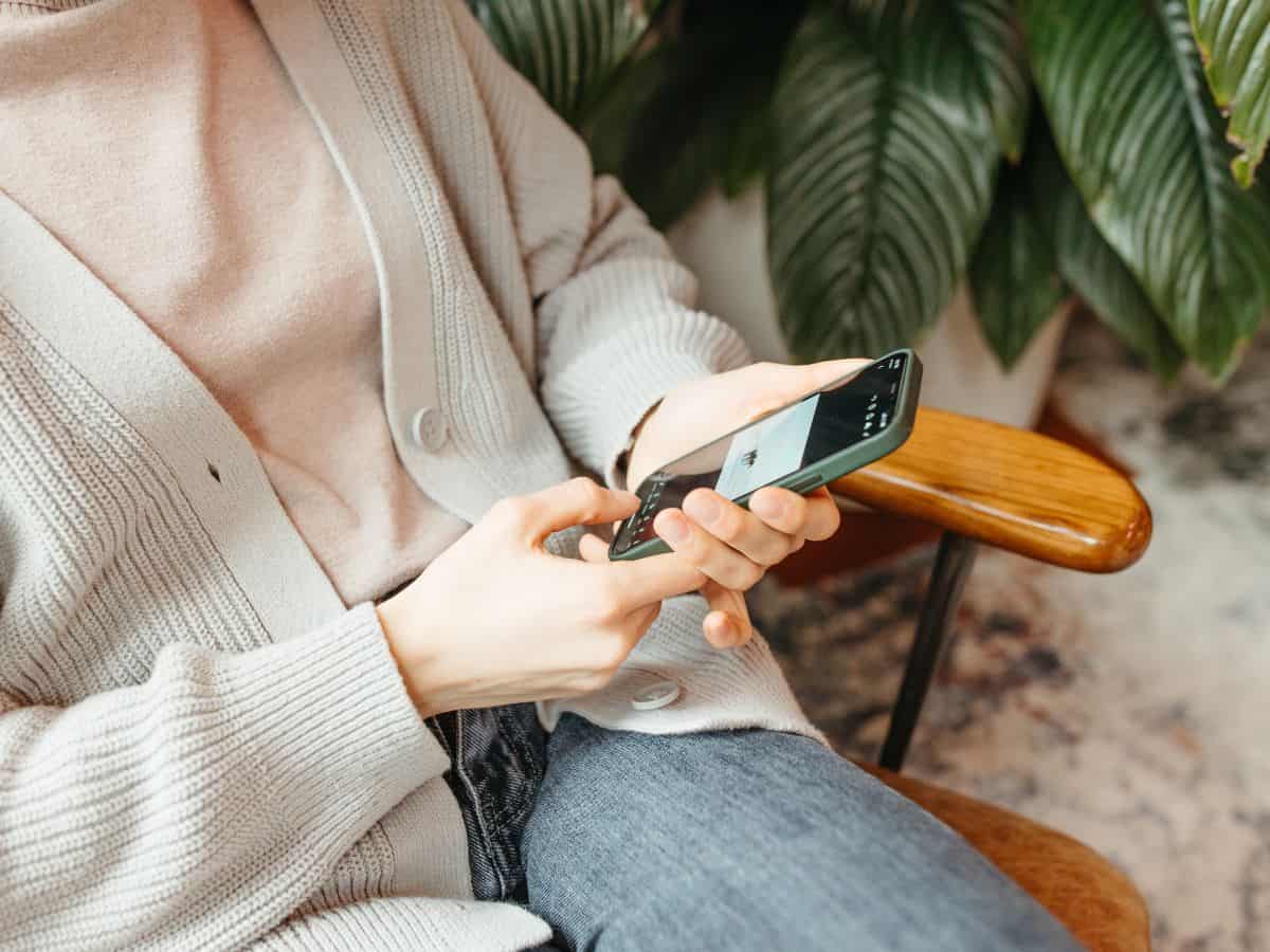 A person holding a smartphone while sitting in a cozy chair, dressed in casual attire. A smartphone is a versatile tool and a must-have on your California packing list for navigation, communication, and entertainment.