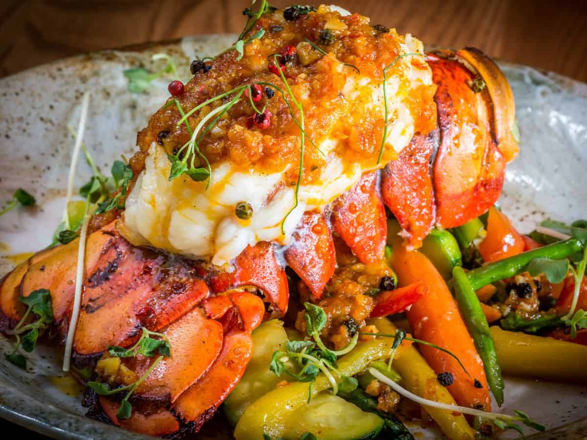 A beautifully presented lobster tail covered in a flavorful sauce, accompanied by vibrant vegetables, embodying the indulgence of Best Seafood In Southern California. This gourmet dish is both visually stunning and delicious.