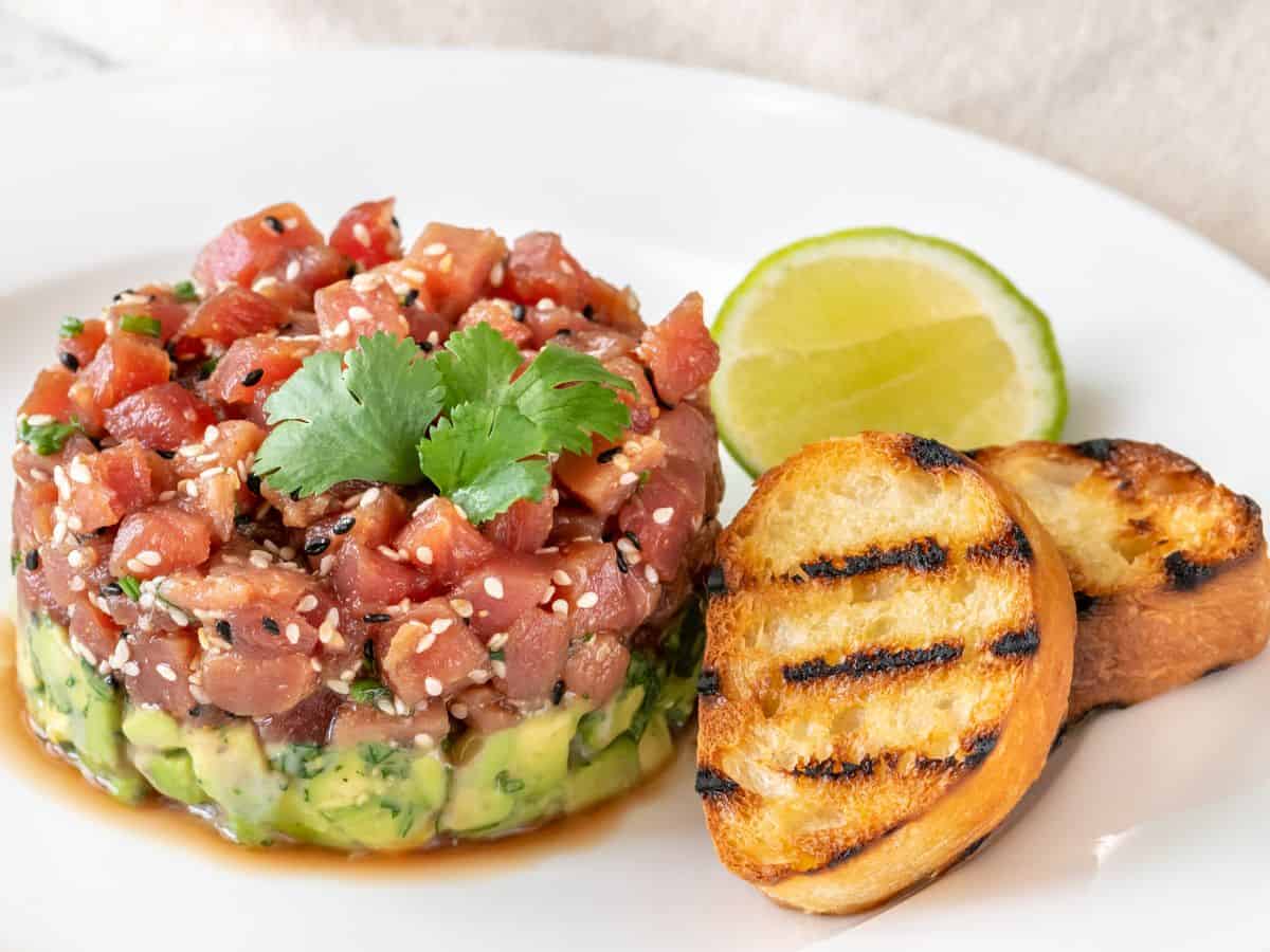  A tower of fresh tuna tartare on a bed of avocado, garnished with sesame seeds and served with grilled bread, illustrating the fusion of freshness and innovation in Best Seafood In Southern California. A refreshing and light seafood option.