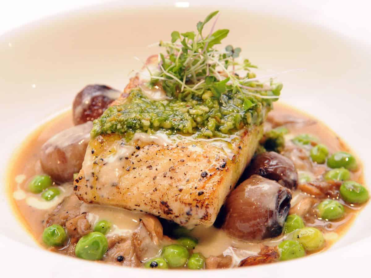 : A fillet of grilled fish topped with a vibrant pesto sauce, served alongside mushrooms and peas, demonstrating the quality and craftsmanship of Best Seafood In Southern California. This dish brings together freshness and bold flavors.