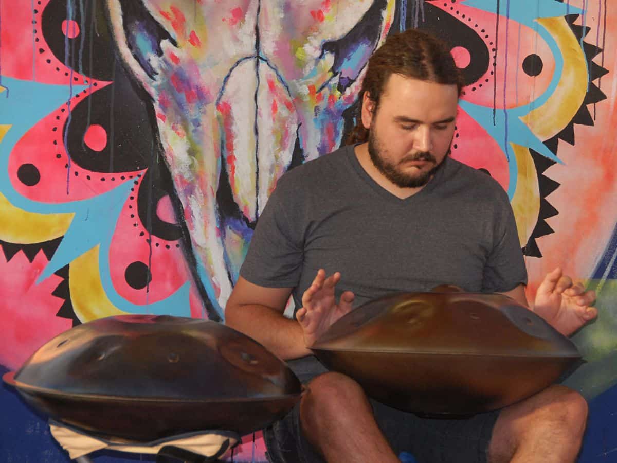 A man playing a handpan at the Joshua Tree Music Festival, surrounded by vibrant street art. Experiencing live music at this annual festival is a great option for things to do in California in October, blending creativity, community, and music under the desert sky.