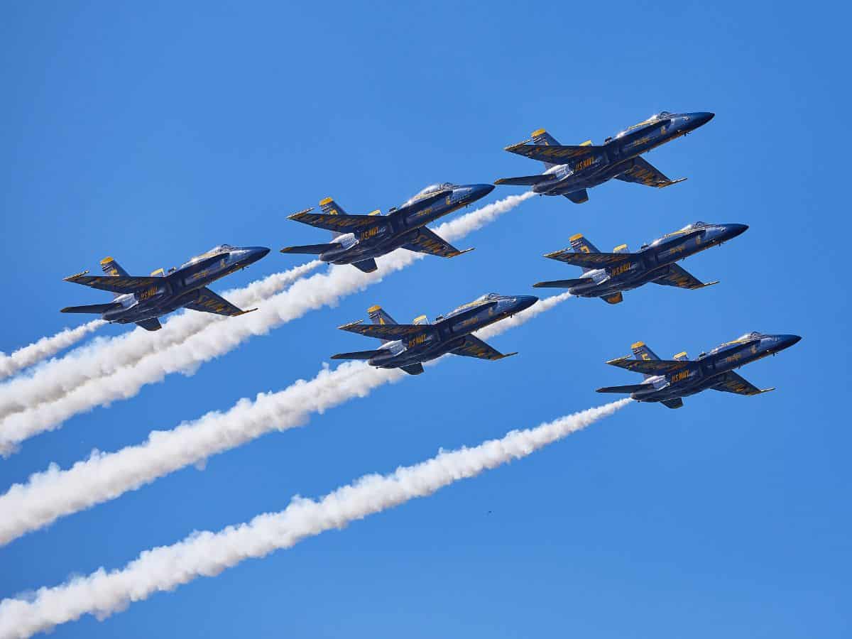 A formation of six blue and yellow fighter jets flying in perfect synchronization, leaving white smoke trails against a clear blue sky. Experiencing the San Francisco Fleet Week air show is one of the exhilarating things to do in California in October, showcasing aerial displays and military demonstrations.