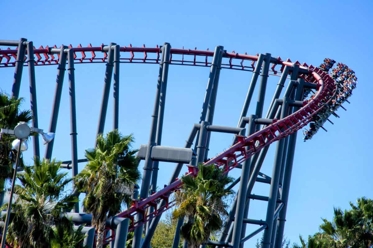 A thrilling roller coaster ride in Santa Clarita, California, with vibrant red tracks looping against a clear blue sky and palm trees in the background. This amusement park scene adds excitement to the Los Angeles to Yosemite road trip, offering an adventurous stop along the way.