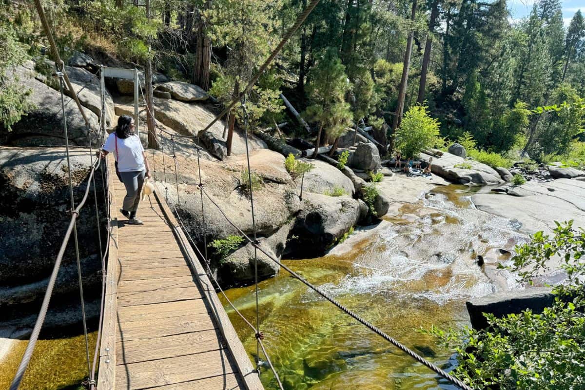 A scenic suspension bridge over a flowing creek in Wawona, Yosemite National Park, surrounded by tall pines and smooth rock formations. A tranquil yet adventurous stop on the Los Angeles to Yosemite road trip, offering stunning views and hiking opportunities.