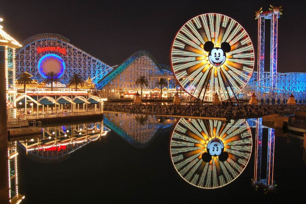 Nighttime view of Disneyland California Adventure park featuring the lit-up Ferris wheel and roller coaster reflecting in the water, highlighting vibrant and fun things to do in Los Angeles.
