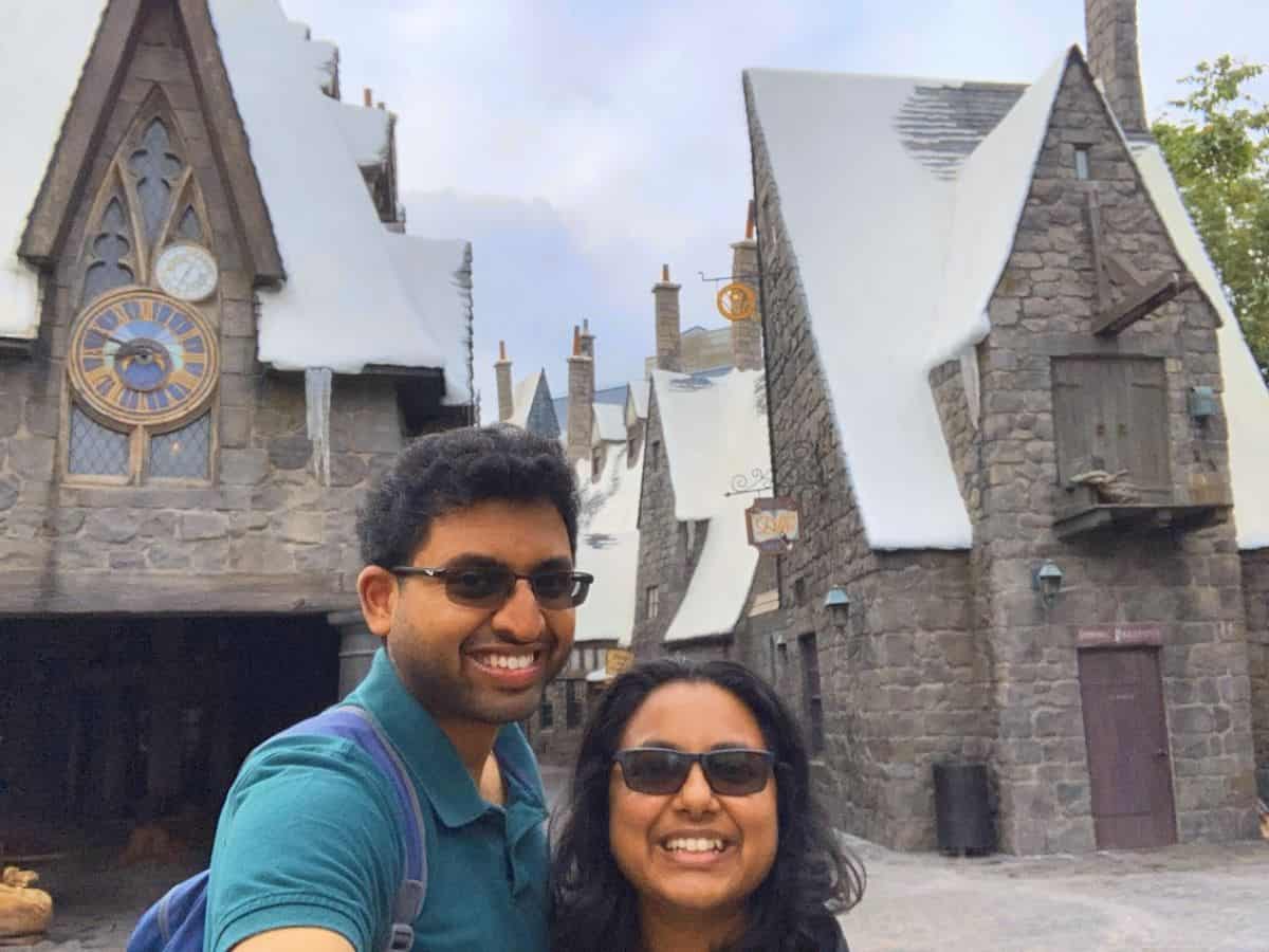 Kiran and Shreeyeh taking a selfie in front of the stone buildings and snowy rooftops of Hogsmeade Village at Universal Studios Hollywood.