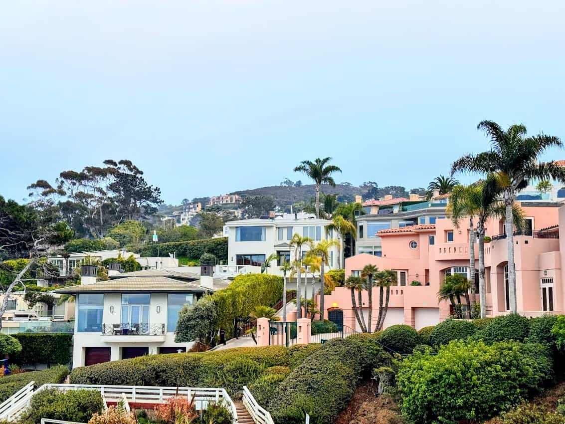 A picturesque neighborhood in La Jolla, San Diego, showcasing pastel-colored houses, lush greenery, and palm trees on a hillside.