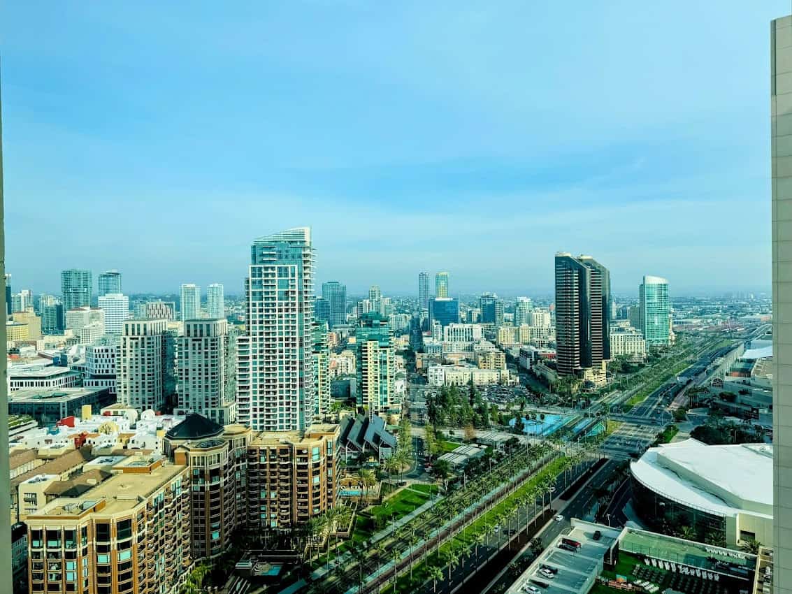 A daytime aerial view of downtown San Diego's skyline, including modern high-rise buildings and waterfront areas, as seen from the Manchester Grand Hyatt.
