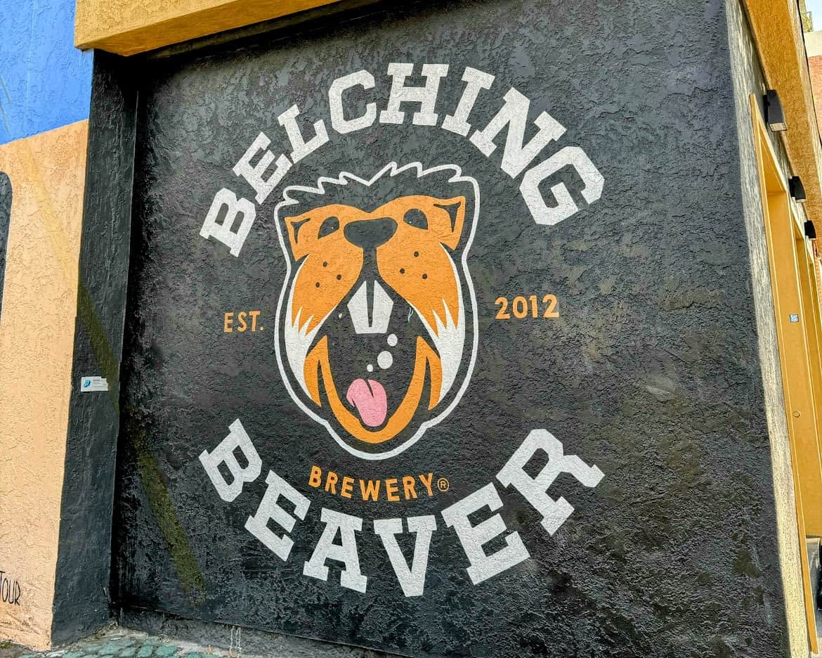 A mural on a black wall featuring the Belching Beaver Brewery logo, with a cheerful beaver illustration and the text "Est. 2012."