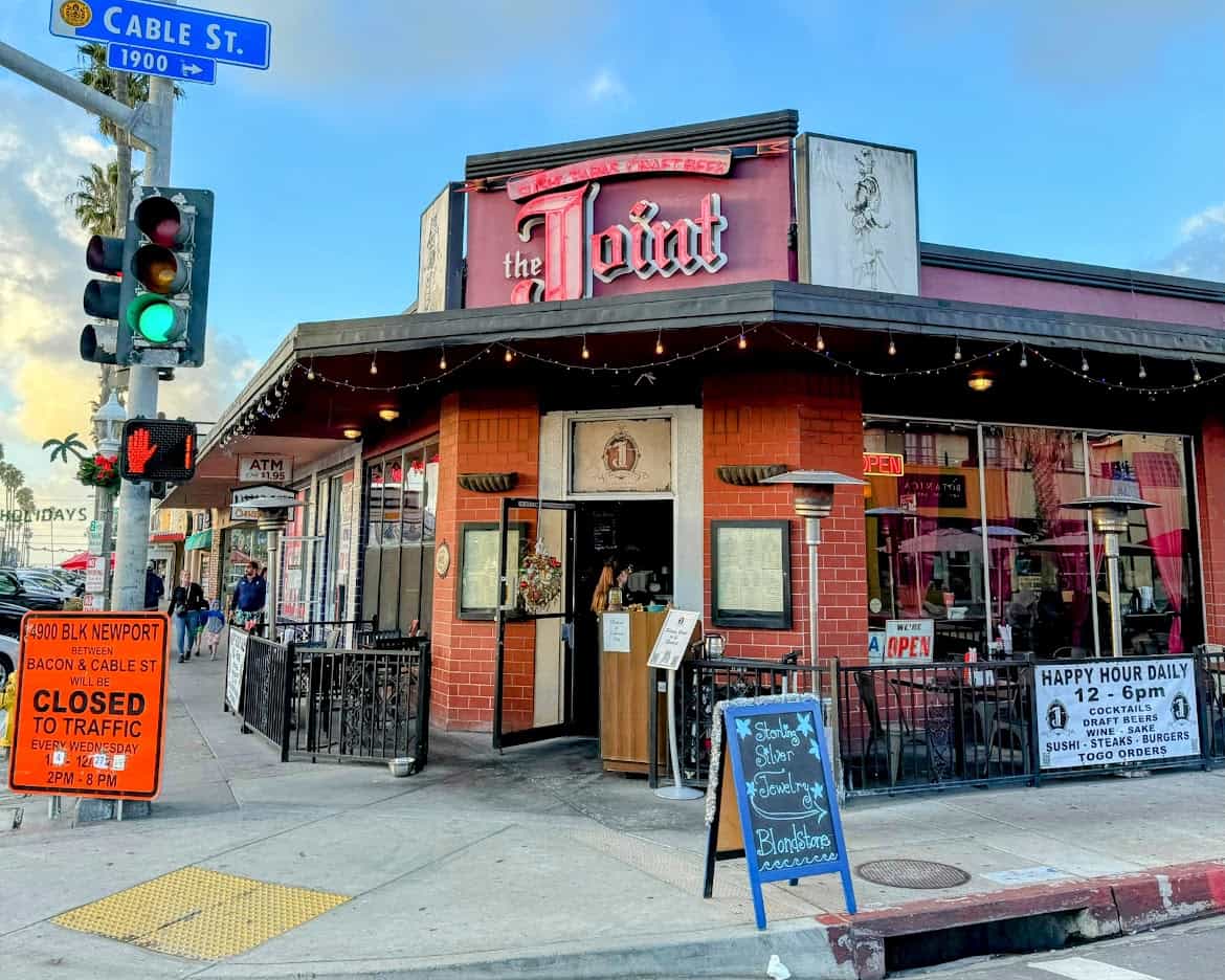 The Joint, a corner restaurant and bar in Ocean Beach, with an outdoor seating area surrounded by string lights. The vintage-style sign and decor create a cozy, vibrant atmosphere.