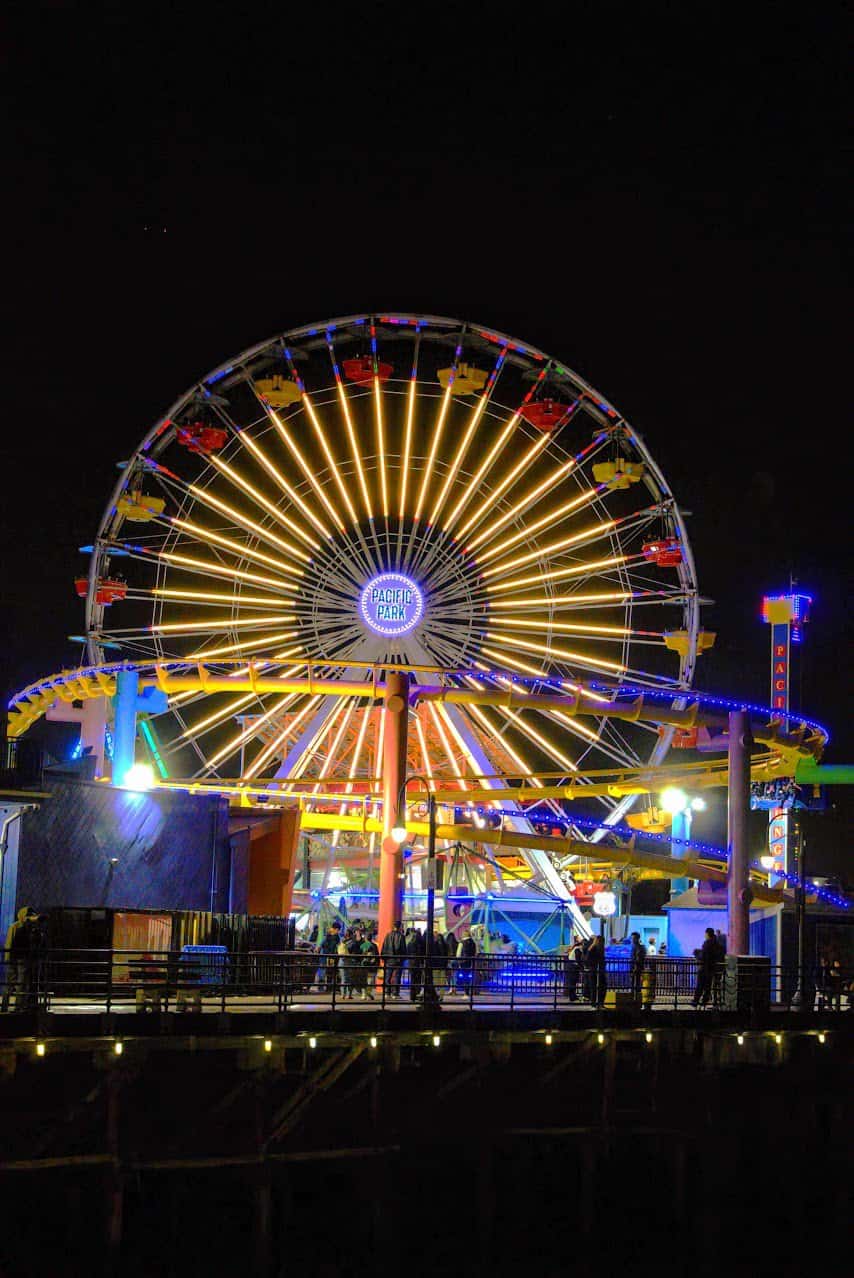 A vibrant Ferris wheel at Pacific Park on the Santa Monica Pier, glowing with colorful lights against a dark night sky, creating a lively and festive atmosphere.