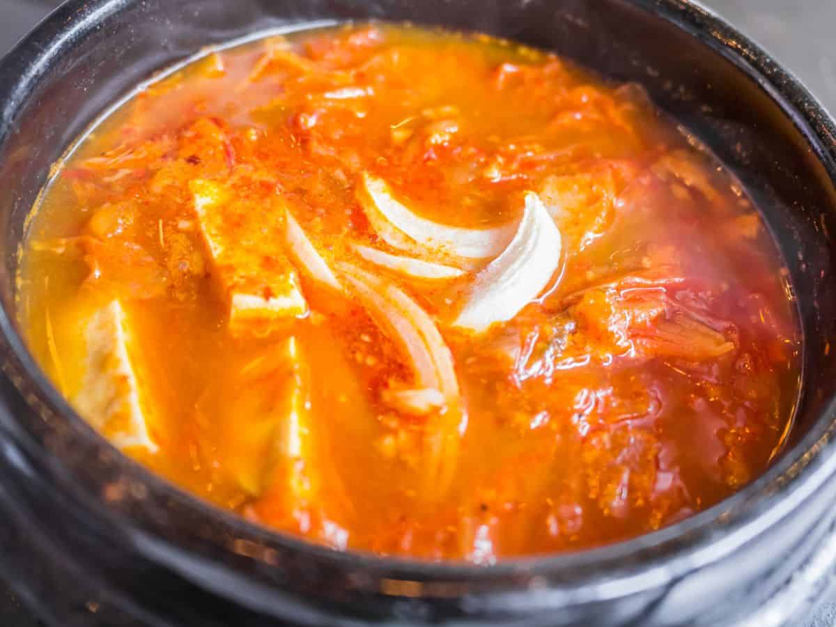 A steaming hot pot of spicy soup with tofu, onions, and vibrant red spices. The boiling broth captures the essence of the fiery and savory dishes often served at hot pot restaurants in San Francisco.