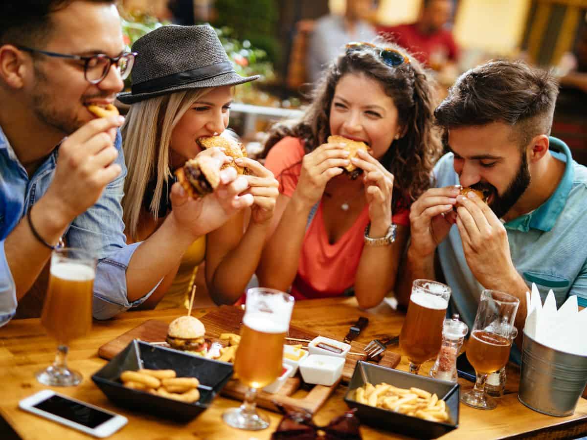 A group of friends laughing and enjoying burgers and fries at an outdoor table with drinks, symbolizing the diverse food scene in Los Angeles as compared to the more traditional offerings in Seattle in the Seattle vs Los Angeles comparison.