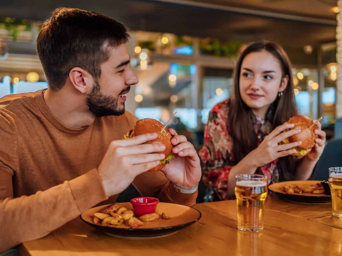 A man and woman sit across from each other in a casual dining setting, enjoying burgers and fries. The friendly atmosphere captures the essence of food culture comparisons, whether it's a burger in a Los Angeles vs New York diner.