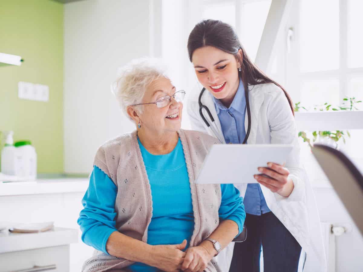 A friendly doctor showing information on a digital tablet to an elderly woman, both smiling in a bright medical office. This image represents healthcare services in Seattle vs. San Francisco, focusing on patient care, medical professionalism, and the quality of health services.