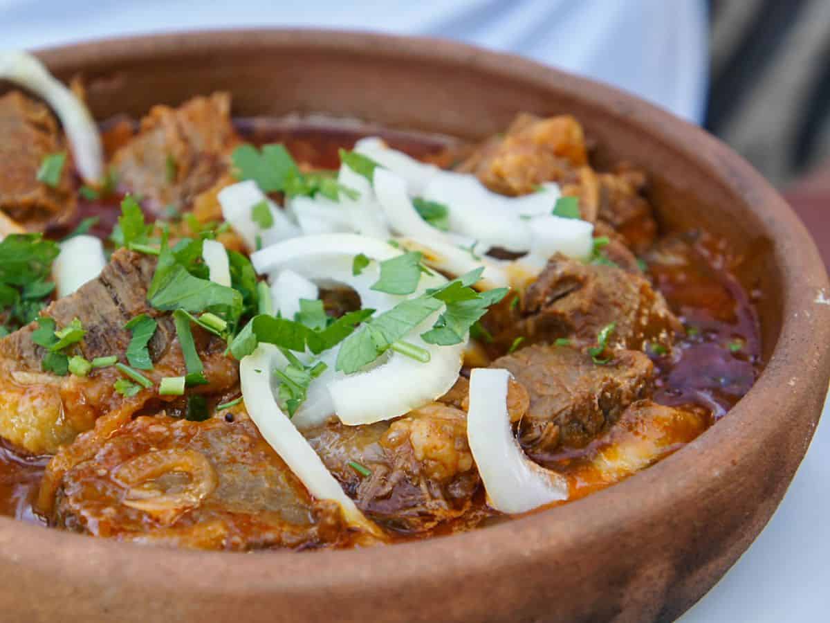 A rustic clay pot filled with tender pieces of beef, garnished with fresh onion slices and herbs. The hearty dish encapsulates the rich, slow-cooked essence of traditional hot pot in San Francisco offerings.