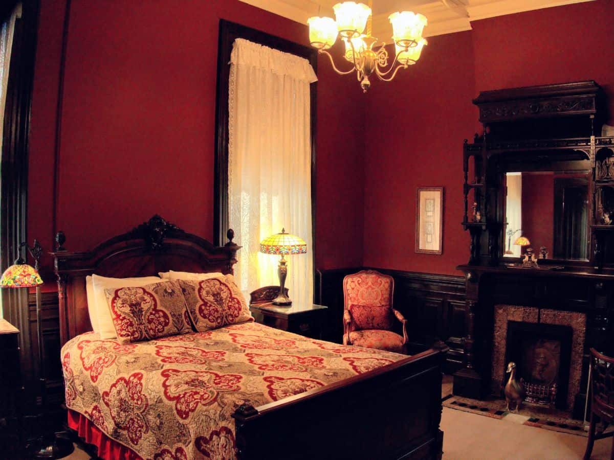 A vintage-style bedroom with rich red walls, an ornate bed, and classic wooden furniture, showcasing the type of unique and charming lodging options available in San Francisco, highlighting the differences in accommodation styles between San Francisco vs Los Angeles.