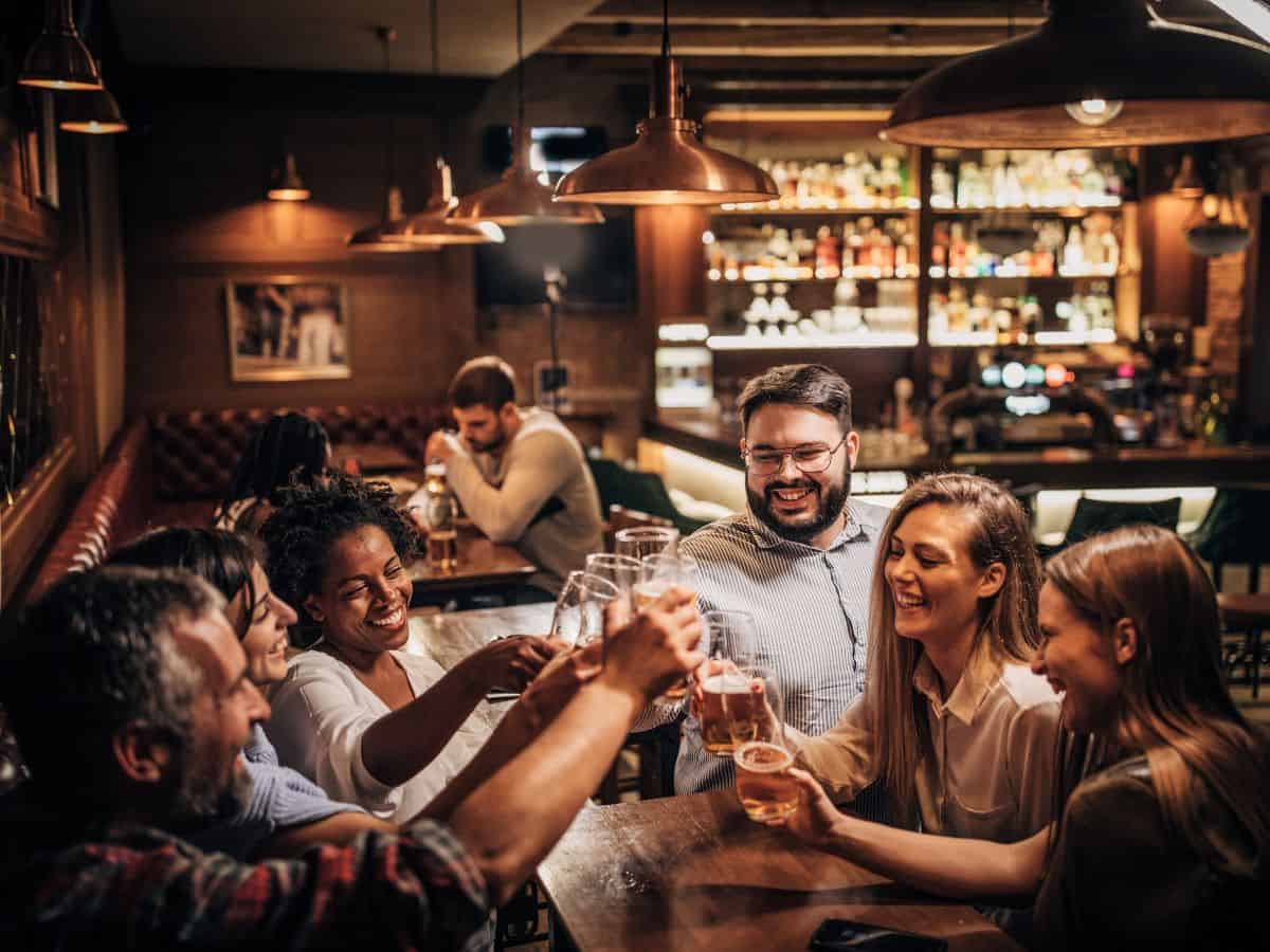 A group of friends celebrating together at a cozy, warmly lit bar, raising their glasses for a toast. This image reflects the nightlife and social culture in Seattle vs. San Francisco, emphasizing the vibrant social scenes and communal gatherings in both cities.