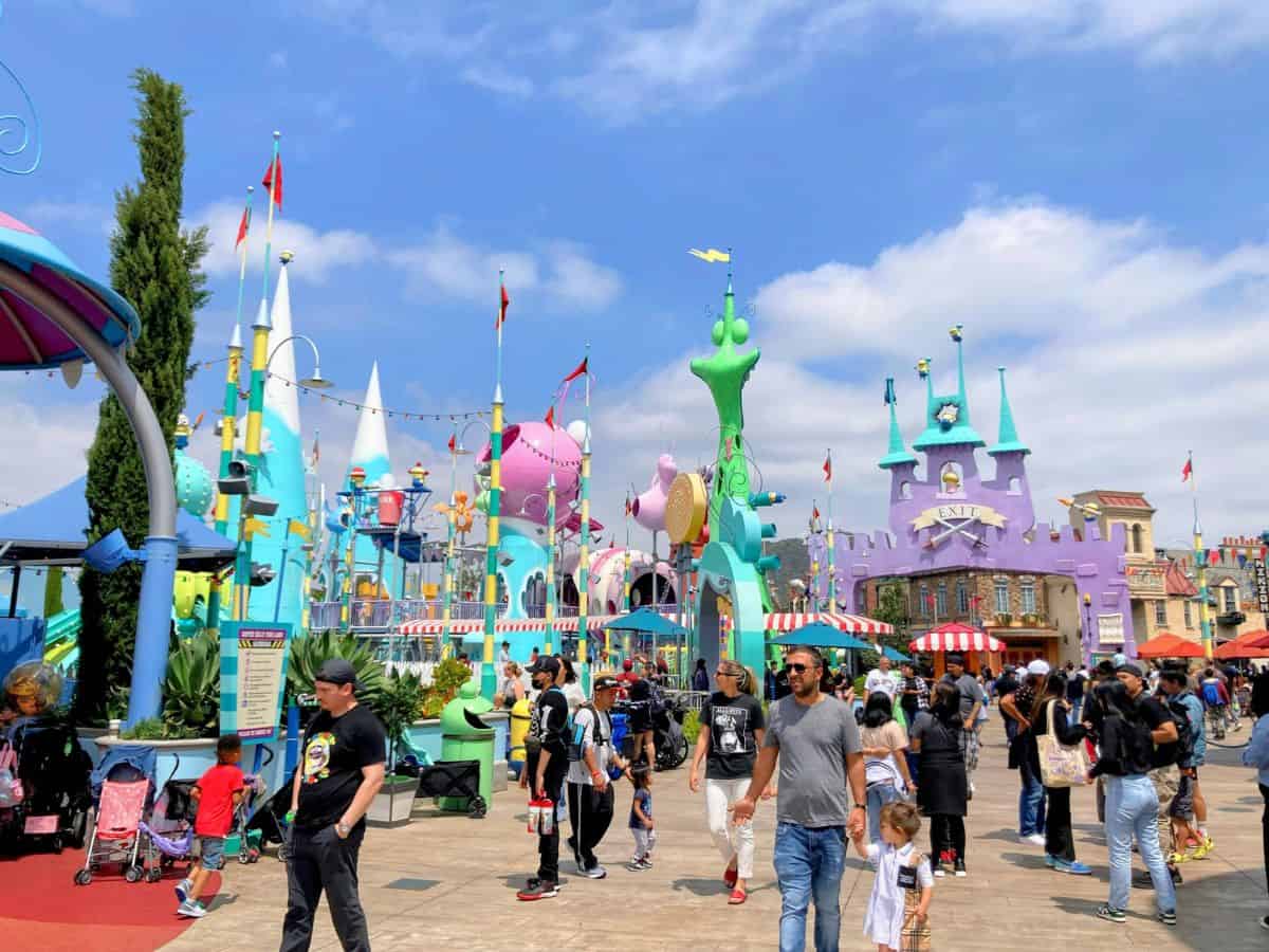 A colorful, lively theme park scene in Los Angeles with various whimsical buildings, playful structures, and people enjoying the attractions, representing the bustling population and diverse recreational opportunities found in Los Angeles in contrast to San Francisco.