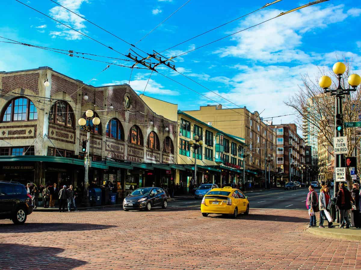 A busy street in Seattle’s Pike Place Market with cars, pedestrians, and historic brick buildings, highlighting the city’s smaller, more intimate population compared to Los Angeles in the Seattle vs Los Angeles population comparison.
