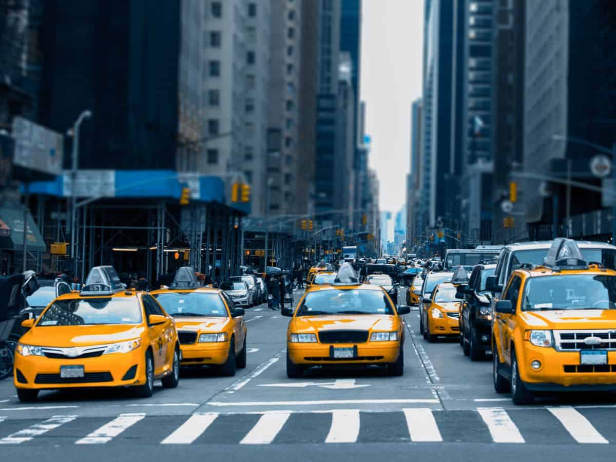A bustling New York City street filled with iconic yellow taxis and high-rise buildings. The dense traffic and urban energy represent the essential role of public transportation, a key comparison point between Los Angeles vs New York City.
