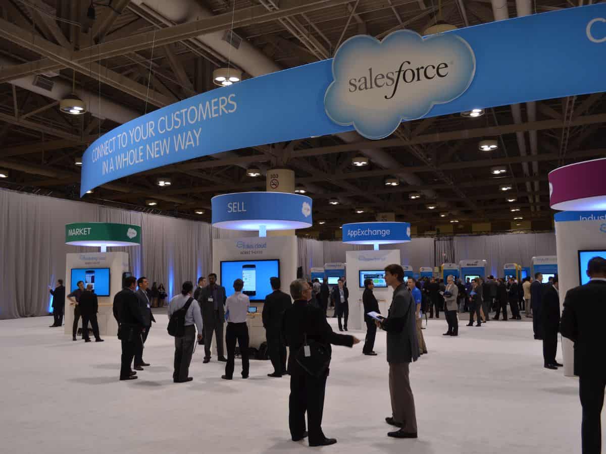 A busy convention hall featuring a Salesforce event with various stalls, attendees conversing, and banners promoting technology and business solutions. This image symbolizes the quality of life in Seattle vs. San Francisco, highlighting professional opportunities, business events, and a dynamic work culture.