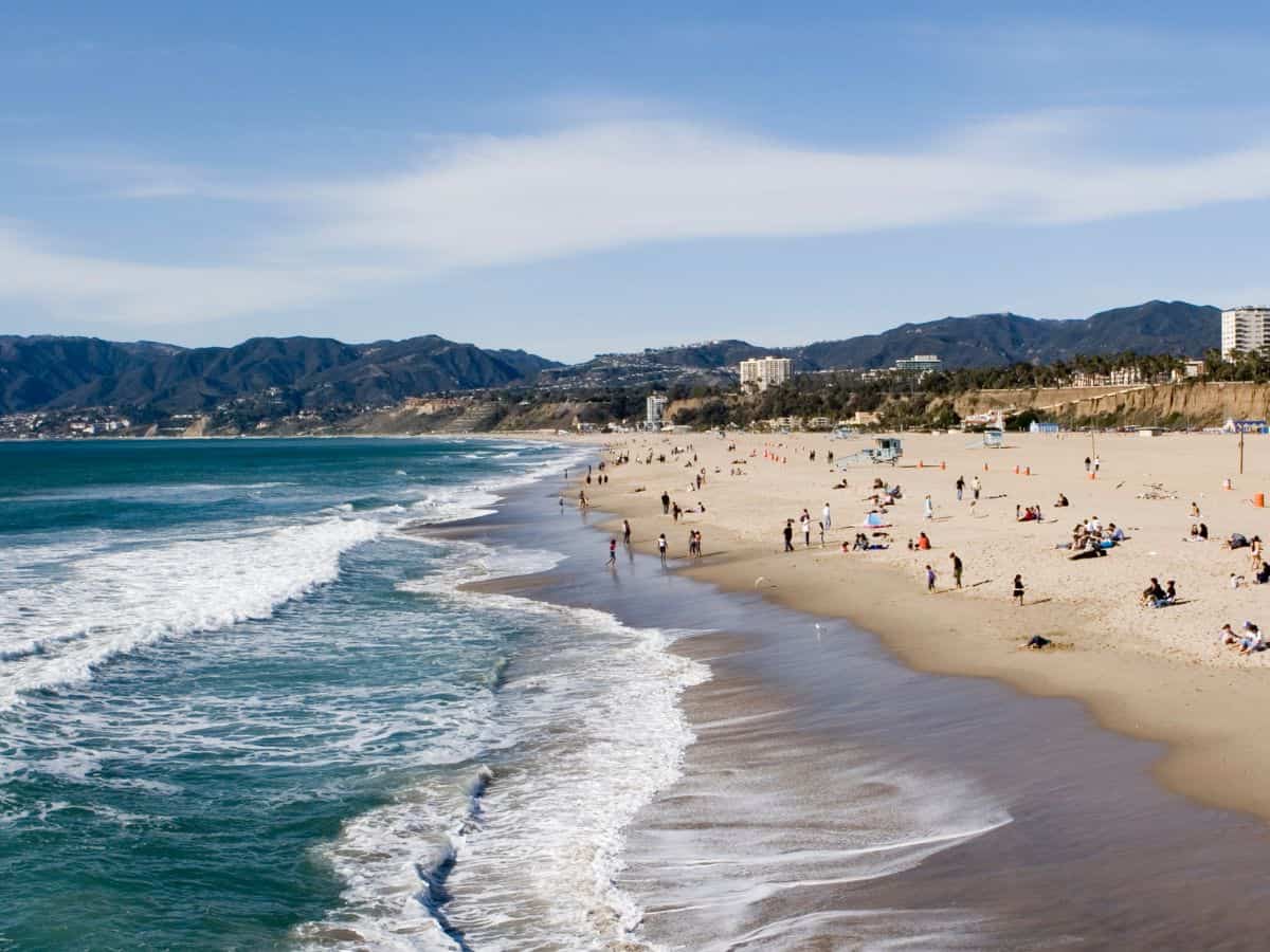 A serene beach scene with waves gently rolling onto the shore as people enjoy the sun and sand. This image highlights the outdoor lifestyle and quality of life often associated with Los Angeles, contrasted with the urban lifestyle of New York City.