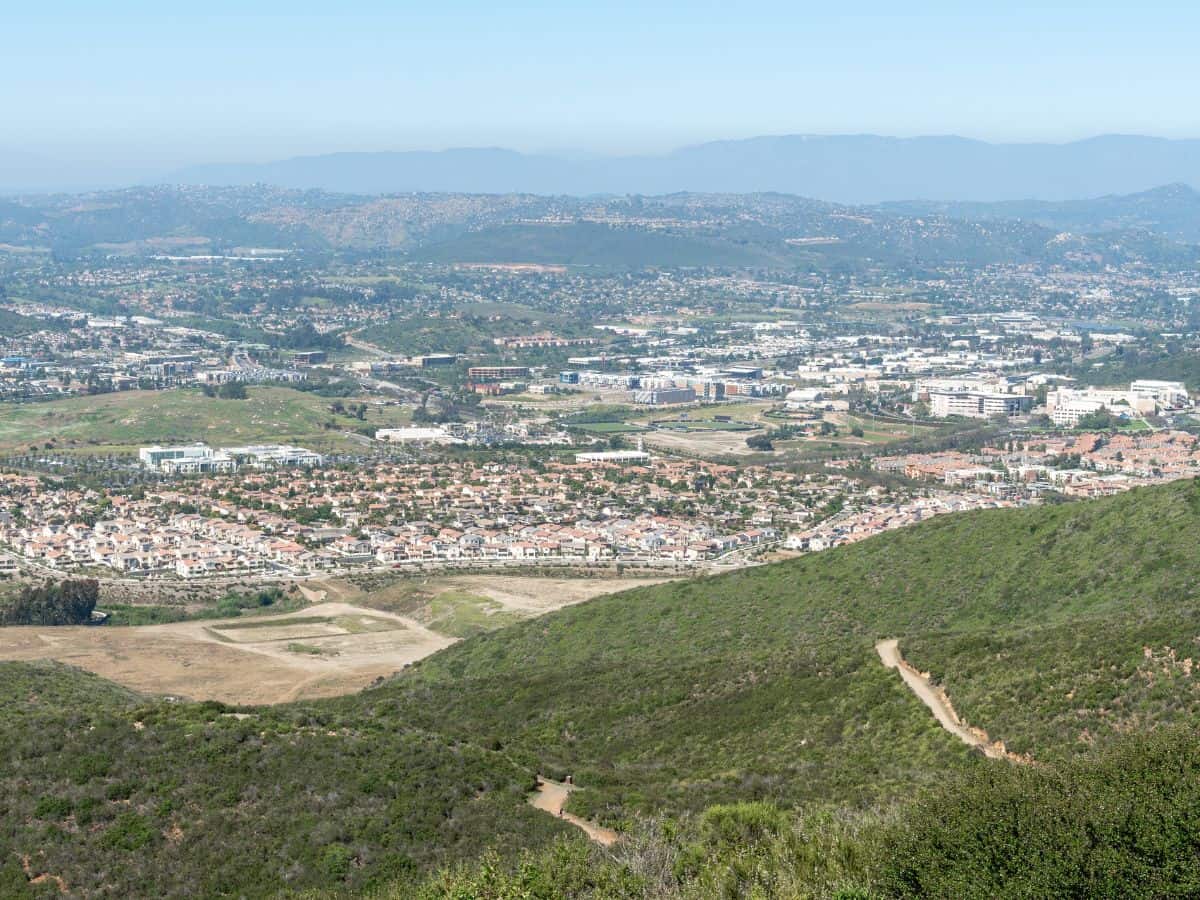 A panoramic view from Double Peak Trail, showcasing a vibrant cityscape nestled among green hills under a bright blue sky.