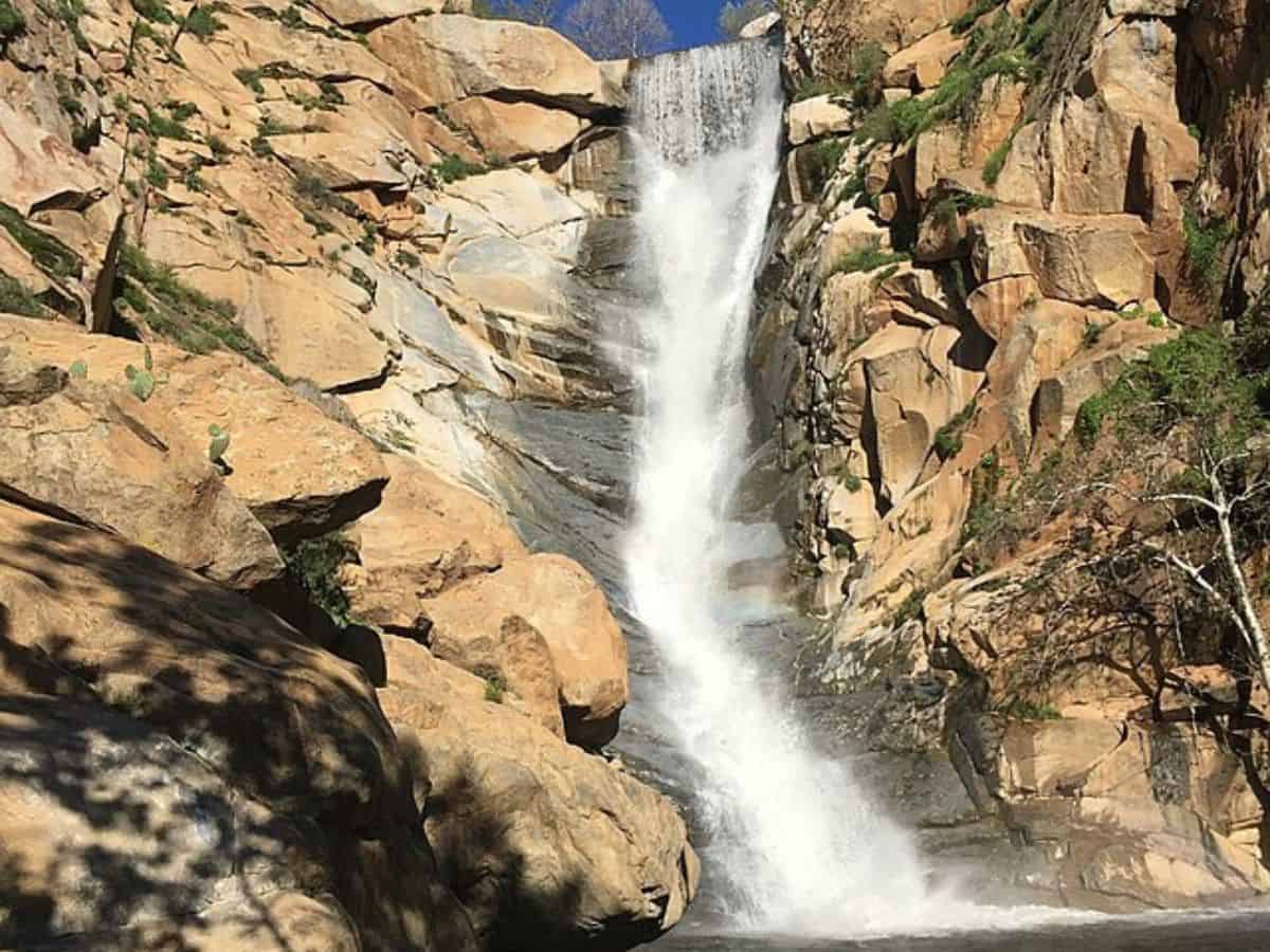 A powerful waterfall cascading down a rocky cliff surrounded by rugged terrain and sparse greenery on Cedar Creek Falls Trail.