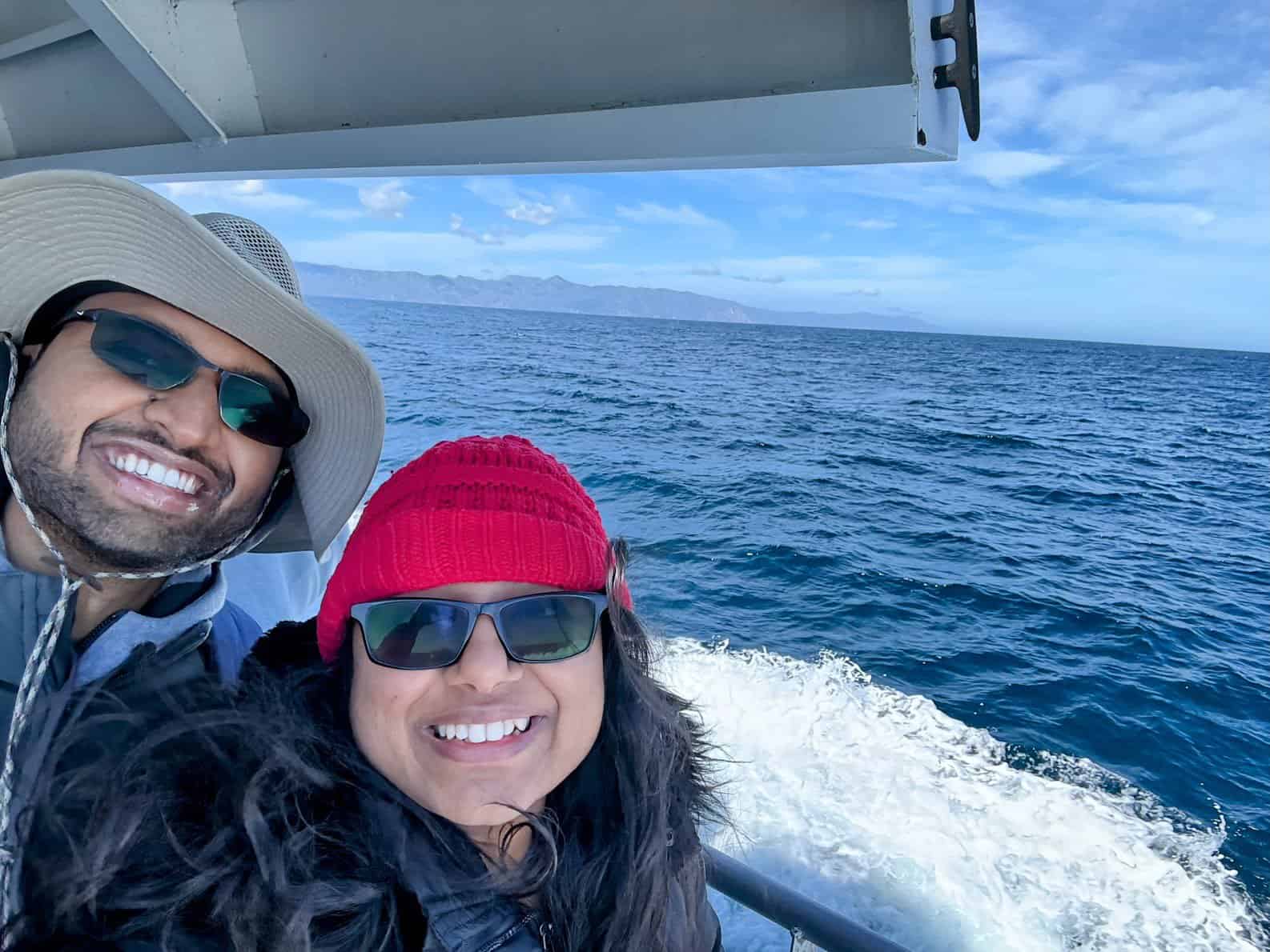 Kiran and Shreeyeh wearing hats and sunglasses on a boat with the ocean in the background, capturing a joyful moment during their journey to Catalina Island.