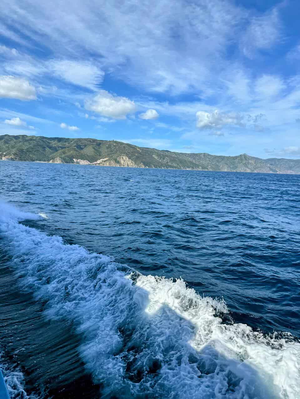 Stunning view of deep blue ocean waves with Catalina Island’s rocky coastline visible in the distance under a clear blue sky. The dynamic water texture highlights the beauty of the journey to Catalina Island.