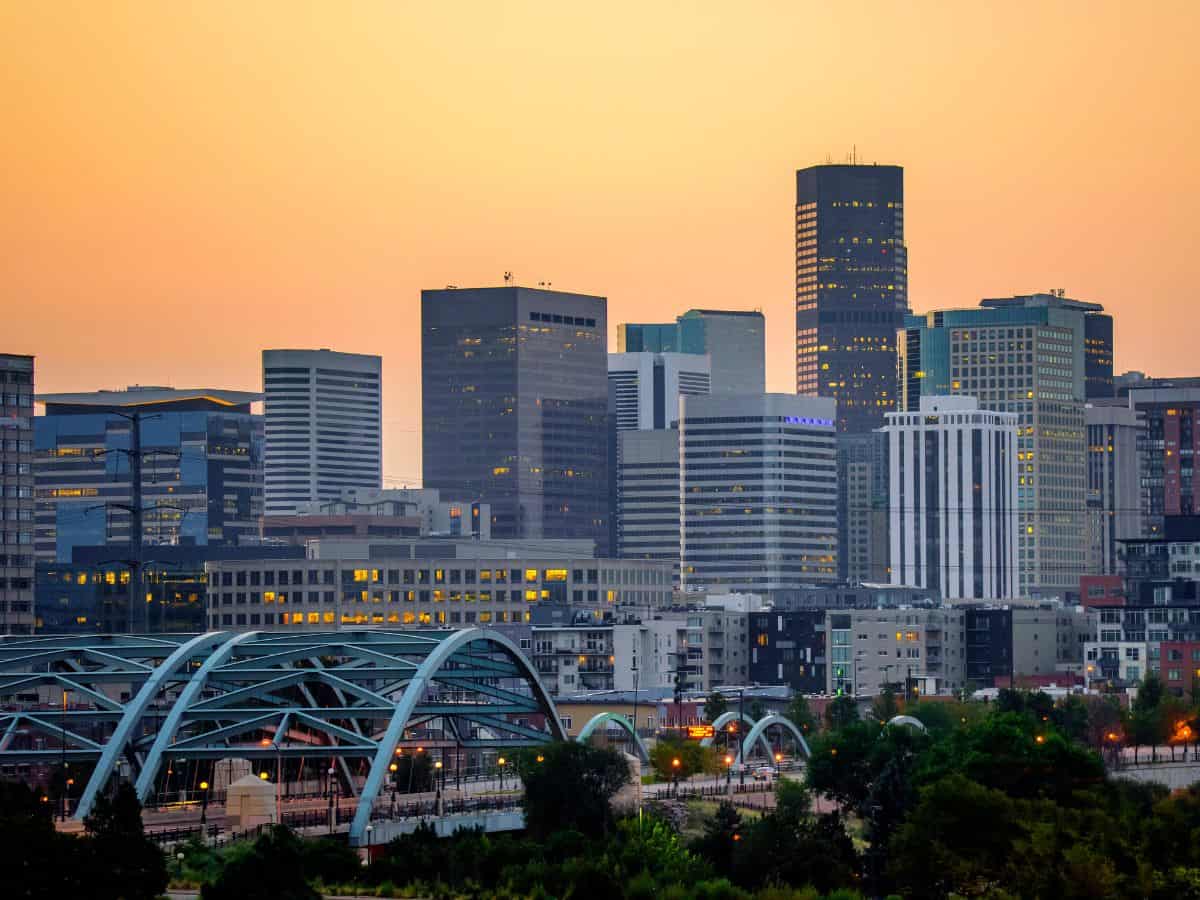 A view of the Denver skyline during sunset with a modern bridge in the foreground. This image represents the cost of living in Denver vs San Francisco, showcasing the city's architecture and urban environment.