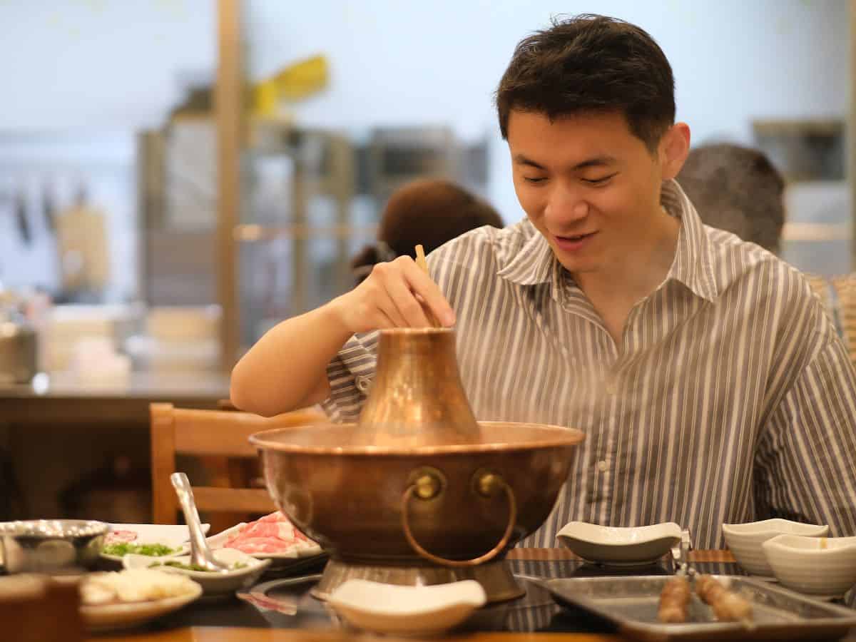 A person enjoying a meal at a restaurant with a steaming hotpot in front of them, representing the diverse food scene in Denver vs San Francisco. The image highlights the culinary experiences available in both cities.