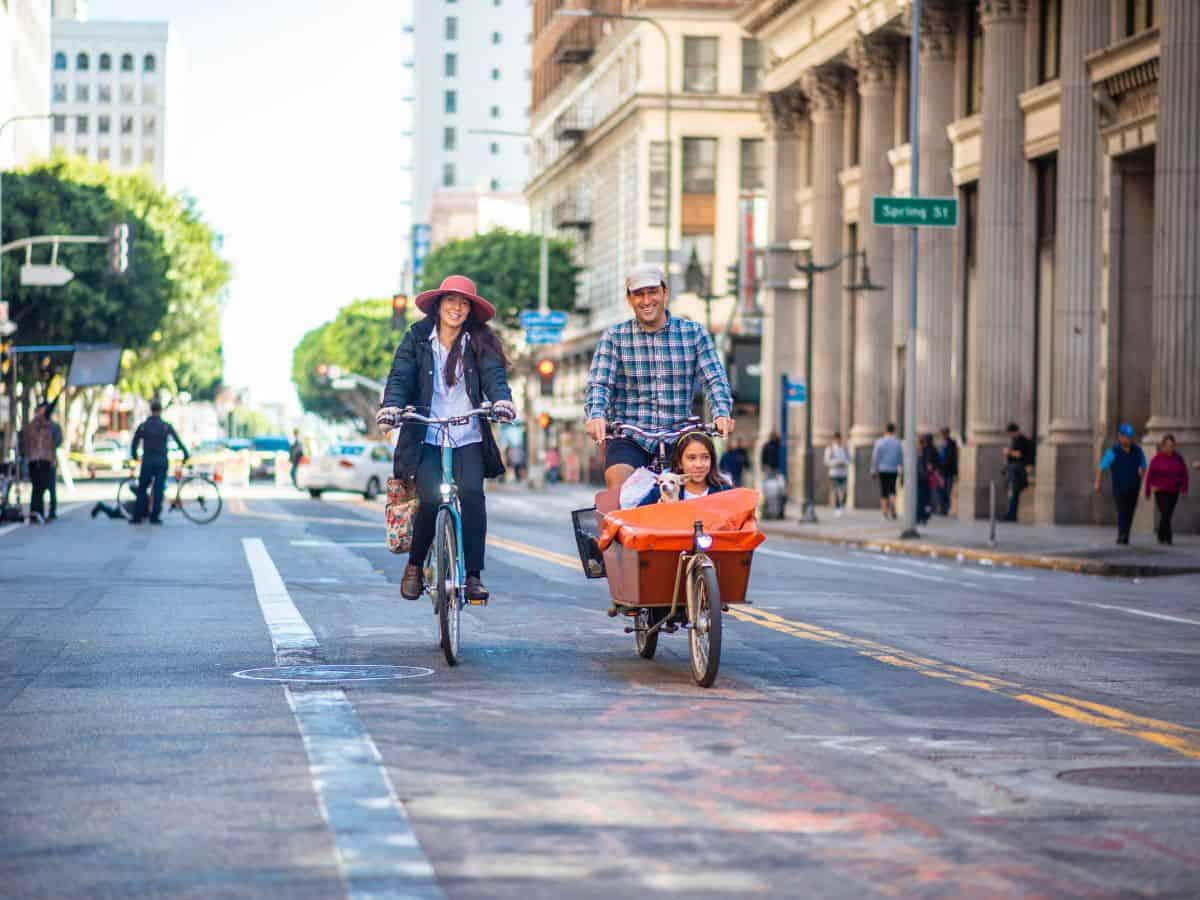  A family cycling down a city street in Los Angeles during the daytime, showcasing a relaxed and safe urban environment. This scene compares the feeling of safety and security in Los Angeles vs Miami.