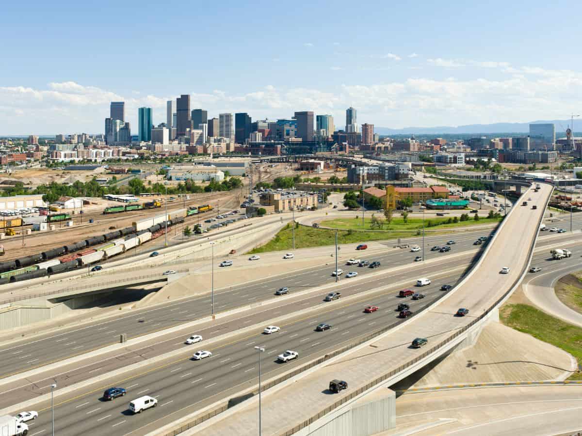 A wide highway filled with moving vehicles leading into Denver’s skyline, representing traffic and commuting challenges in Denver vs San Francisco. The image emphasizes the infrastructure and transportation differences between the two cities.